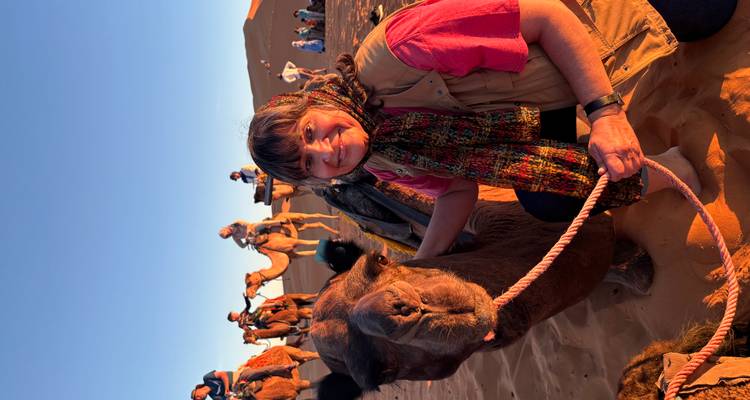Woman posing next to a camel in a desert landscape.