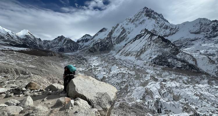 Personne se reposant sur un rocher devant des montagnes enneigées.