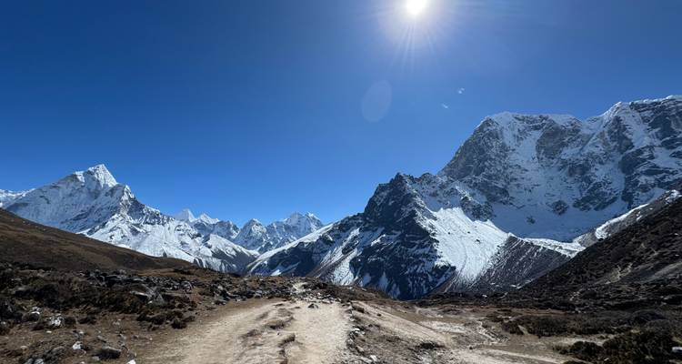 Sentier de montagne avec une vue panoramique sur des sommets enneigés sous un ciel bleu éclatant.