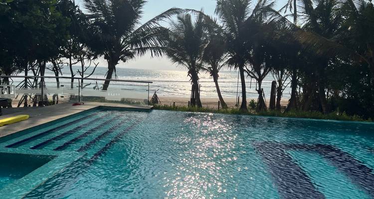 Pool mit Meerblick und Palmen bei Sonnenuntergang.