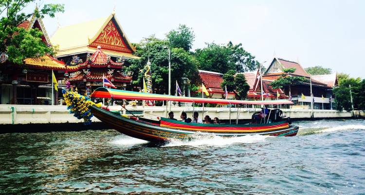 Bateau coloré passant à toute vitesse devant des bâtiments traditionnels thaïlandais.
