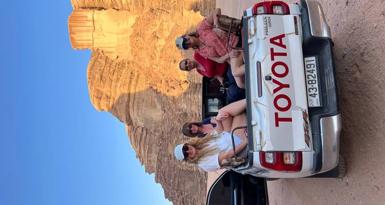 Gruppe von Touristen, die hinten auf einem Pickup-Truck in einer Wüste sitzen.