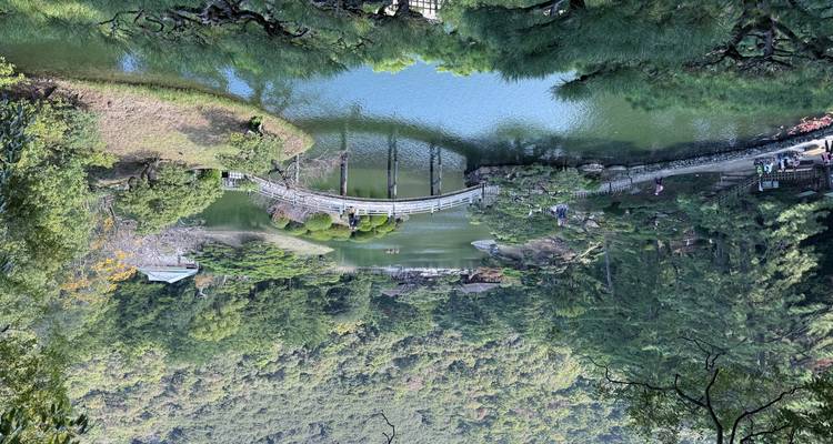 Scenic landscape of a Japanese garden with a bridge over a pond, surrounded by greenery.
