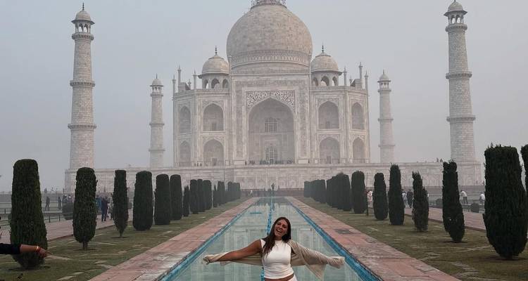 A person posing in front of the Taj Mahal in the morning mist.