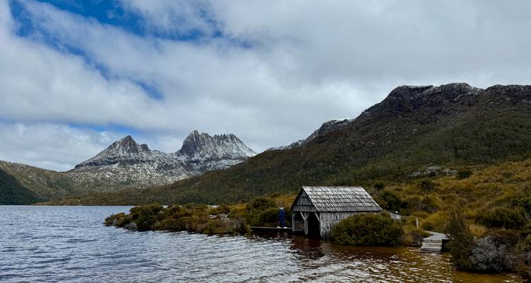 Una casa de botes junto al agua con montañas cubiertas de nieve al fondo.