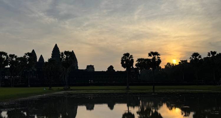 Angkor Wat bij zonsopgang met reflectie in het water en de zon die door de wolken piept.