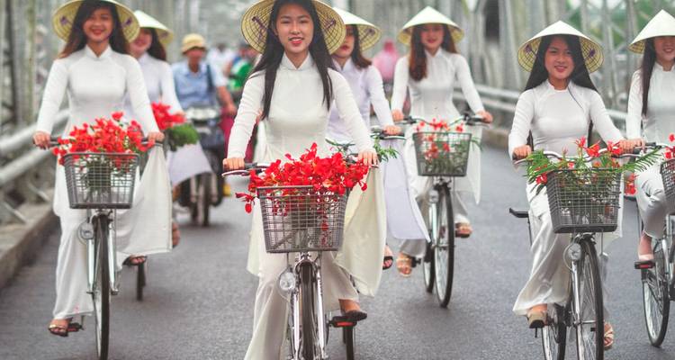 Frauen in weißen traditionellen Kleidern auf Fahrrädern mit Blumen.