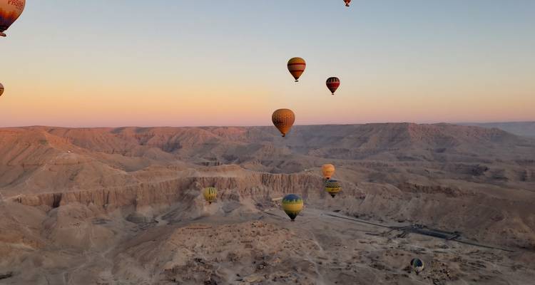 Heißluftballons, die bei Sonnenaufgang über eine Wüstenlandschaft aufsteigen.