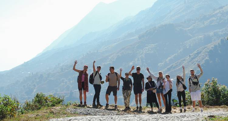 Gruppe von Menschen, die auf einem Wanderweg winken, mit Bergen im Hintergrund.