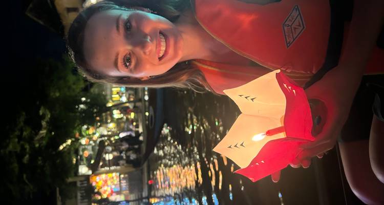 Person, die während eines Festivals eine schwimmende Laterne auf einem Fluss hält.