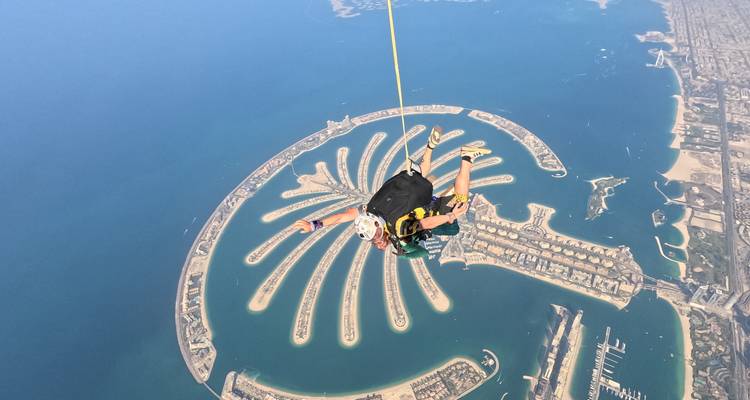 Fallschirmspringer über einer palmenförmigen Insel in klarem blauen Wasser.