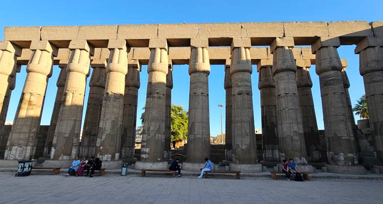 Ancient columns of Luxor Temple with visitors seated below.