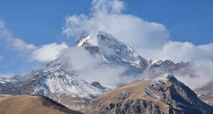Montaña con nieve en la cima con nubes arriba.