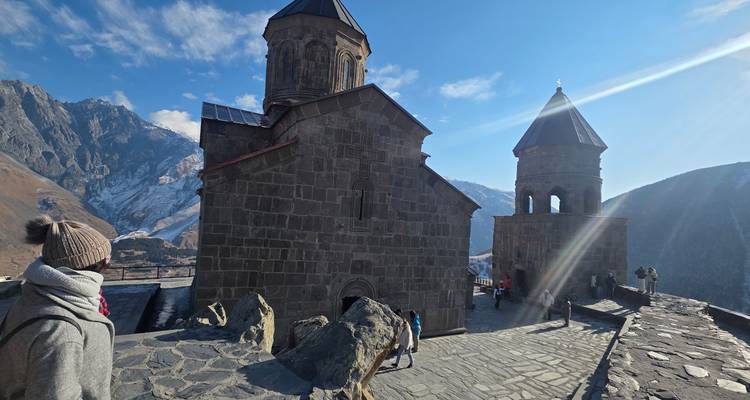 Iglesia de piedra con gente y montañas al fondo.