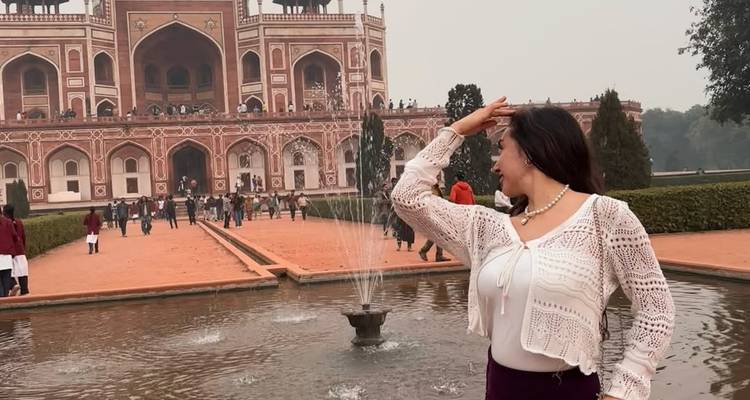 Femme posant devant une structure historique emblématique avec une fontaine.