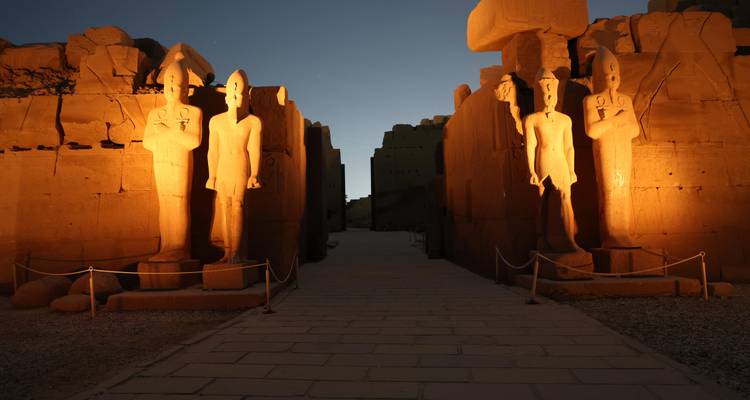 Ancient Egyptian statues illuminated at night.
