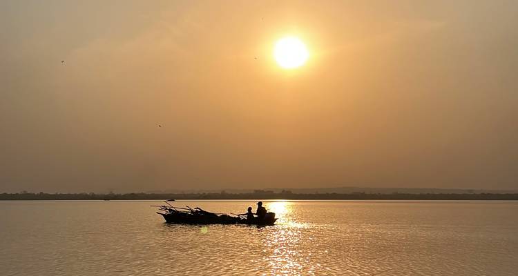 Silueta de un barco en un río tranquilo durante el atardecer.