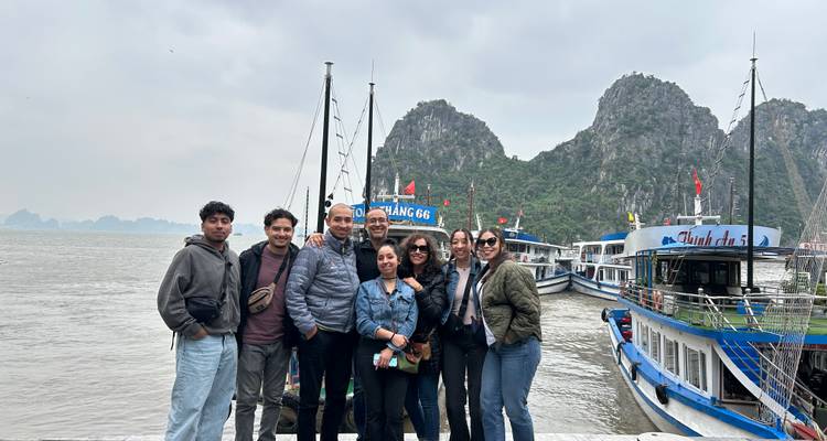 Grupo de personas en un muelle con barcos y formaciones kársticas.