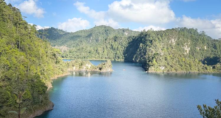 Vista serena del lago con colinas verdes al fondo bajo un cielo brillante.