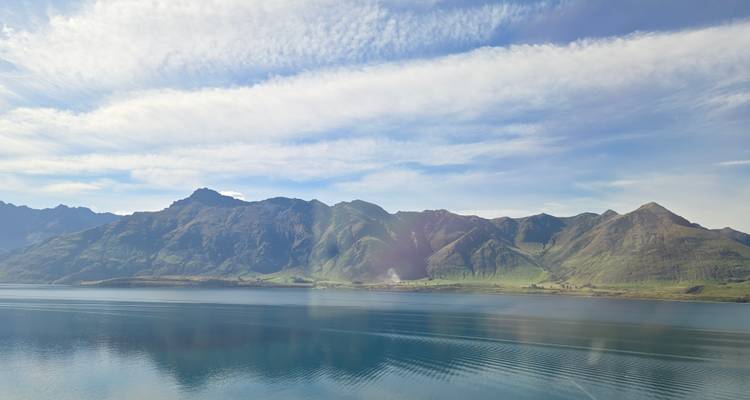 Gebirgskette, die sich in einem ruhigen See unter einem teilweise bewölkten Himmel spiegelt.