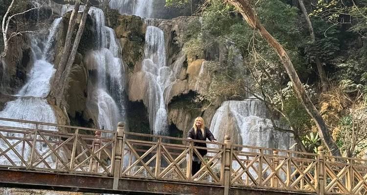 Una mujer parada en un puente de madera con una cascada de fondo.