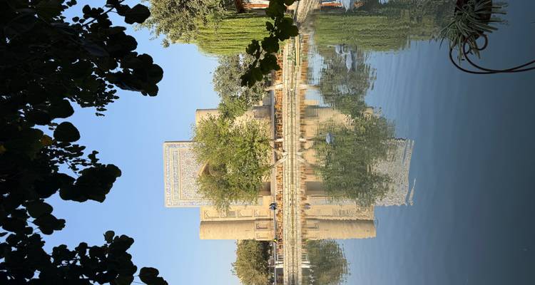 Vista panorámica de un edificio histórico reflejado en un estanque rodeado de árboles.