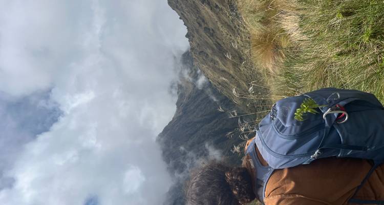 Person mit Rucksack blickt auf bewölkte Berge.