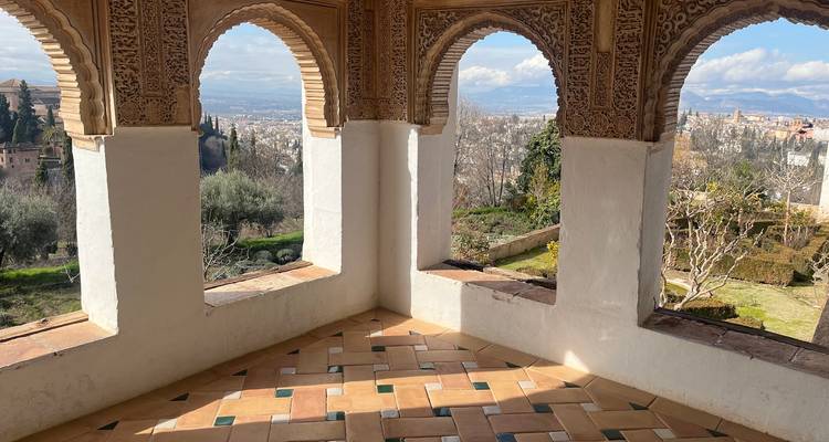 Des arcs mauresques complexes encadrant des vues panoramiques sur les jardins et Grenade depuis l'intérieur du palais de l'Alhambra.