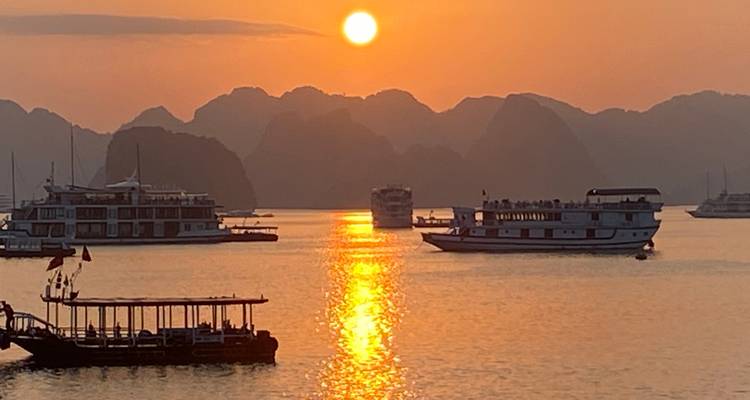 Le soleil doré se couche sur les karsts calcaires et les bateaux de croisière dans la baie d'Halong, Vietnam.
