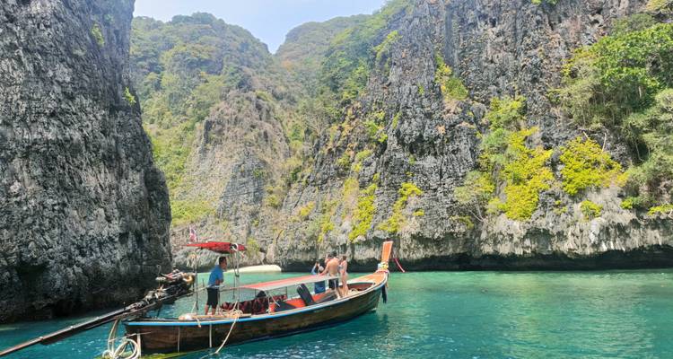 A long-tail boat glides through turquoise water between towering limestone cliffs covered in greenery.