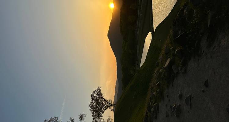 Coucher de soleil serein sur un monticule herbeux et un canal réfléchissant avec des collines lointaines en silhouette.