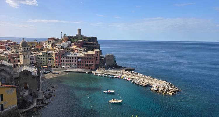 Vue panoramique du port de Vernazza, maisons pastel et tour du château contre la mer Ligure d'un bleu éclatant.