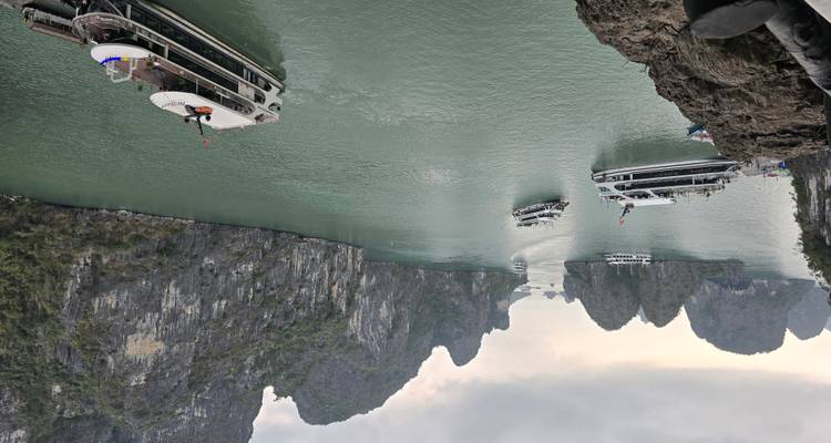 Tourboten varen tussen torenhoge kalkstenen eilanden in het smaragdgroene water van Halong Bay.