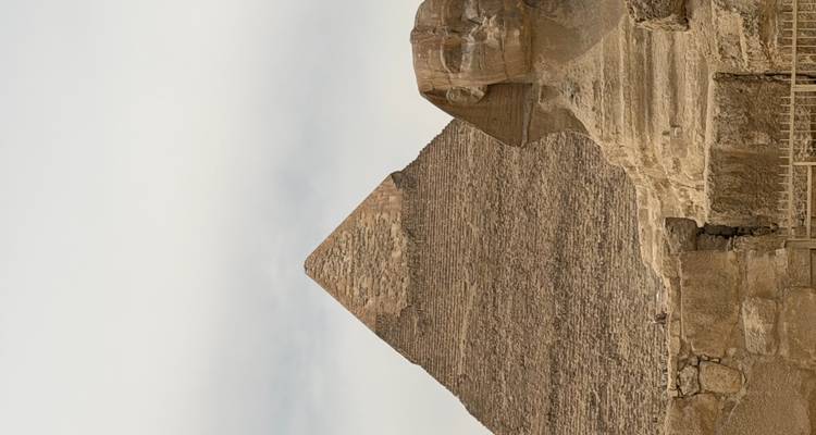 Ikonischer Blick auf die Große Sphinx mit der dahinter aufragenden Chephren-Pyramide unter einem dunstigen Himmel.
