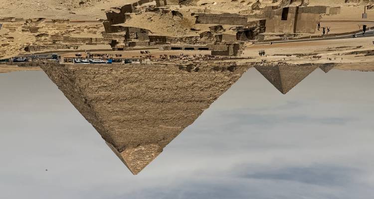 Panoramablick auf die Wüste mit der Großen Pyramide und nahegelegenen Pyramiden unter einem dunsigen Himmel.