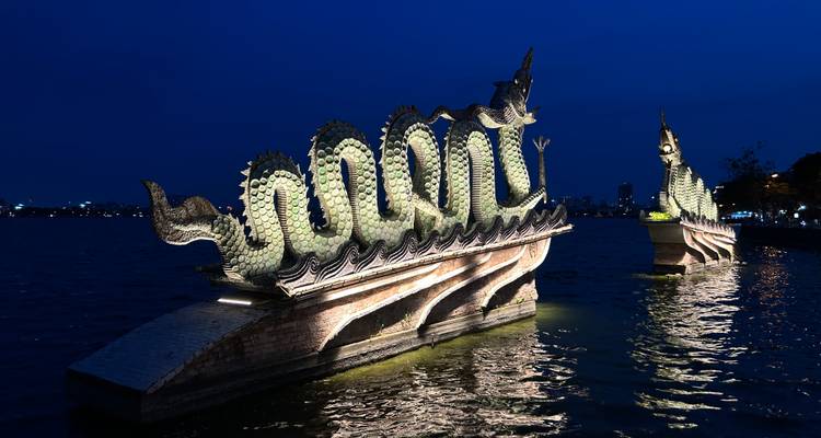 Beleuchtete Drachenboot-Skulpturen, die auf ruhigem Wasser gegen einen tiefblauen Nachthimmel glänzen.