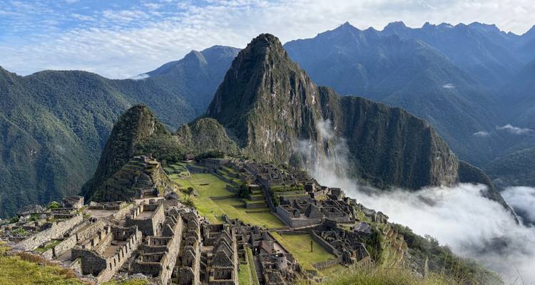 Iconic panoramic view of Machu Picchu ruins perched on a ridge with Huayna Picchu peak and drifting clouds behind.