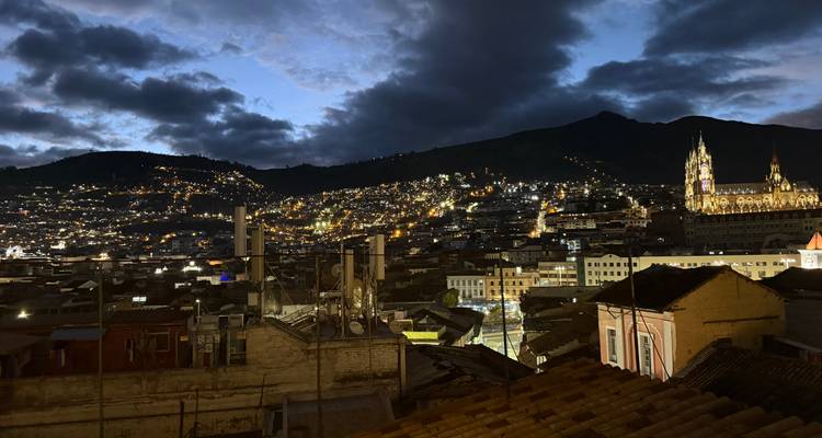 Panorama nocturno de las luces parpadeantes de Quito con la basílica iluminada y la silueta de la montaña.