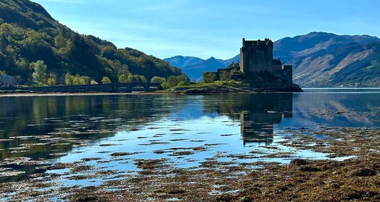 Die ikonische Burg Eilean Donan vor Bergsilhouette und perfekt gespiegelt in ruhigen Gezeitengewässern.