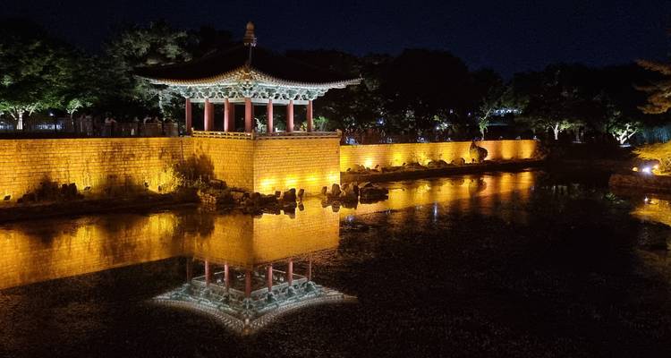 Reflet nocturne d'un pavillon traditionnel et d'un mur de pierre dans un étang tranquille illuminé par des lumières chaudes