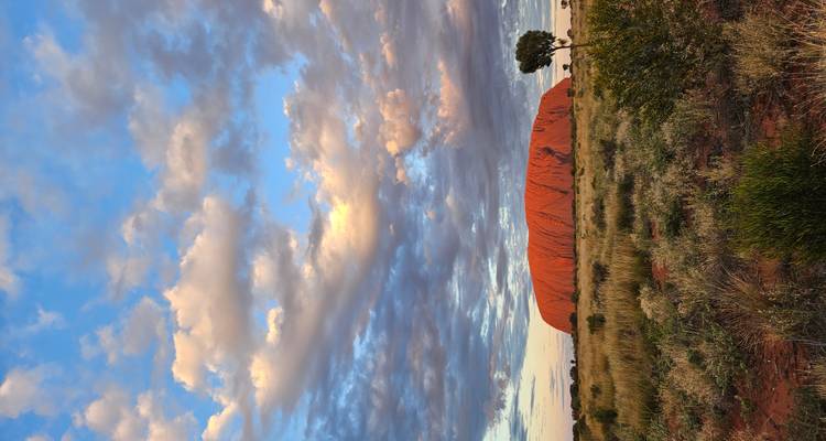 Iconic Uluru rises from the red desert plain beneath dramatic, pastel-lit evening clouds.