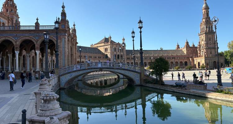 Elegant tiled bridge and soaring towers of Plaza de España reflect in the tranquil canal.