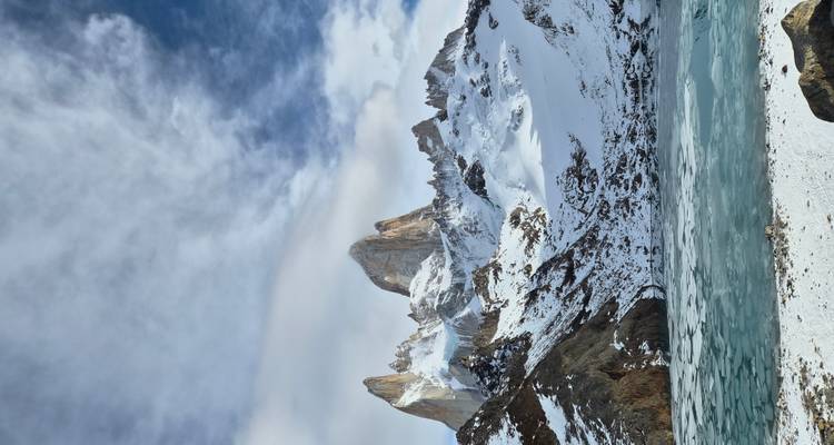 Snow-clad Mount Fitz Roy rises dramatically above a frozen turquoise lagoon under patchy clouds.
