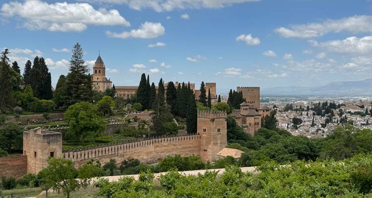 Exuberantes jardines y fortificaciones de la Alhambra con vistas a la ciudad de Granada en un día despejado.