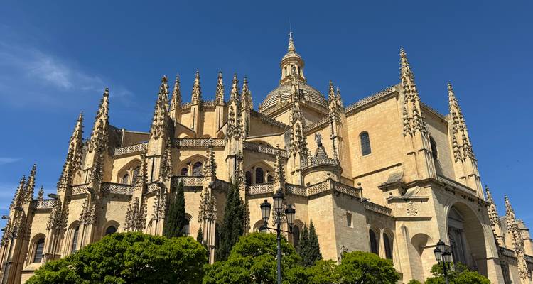 La Catedral Gótica de Segovia se eleva sobre árboles verdes con elaborados pináculos contra cielos despejados.