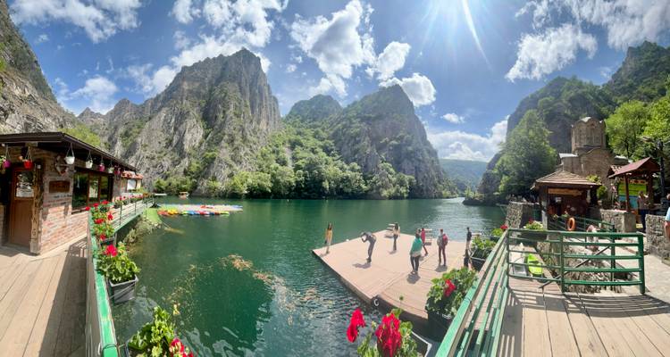 Les visiteurs pratiquent le yoga sur un quai dans le canyon de Matka aux eaux émeraude, encadré par des falaises calcaires imposantes et des fleurs.