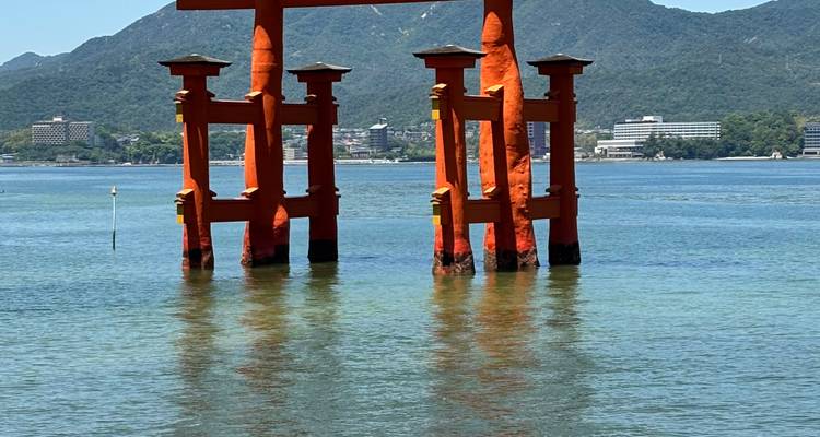 Le célèbre portique torii orange du sanctuaire d'Itsukushima se dressant dans les eaux calmes de la baie avec les montagnes en arrière-plan.
