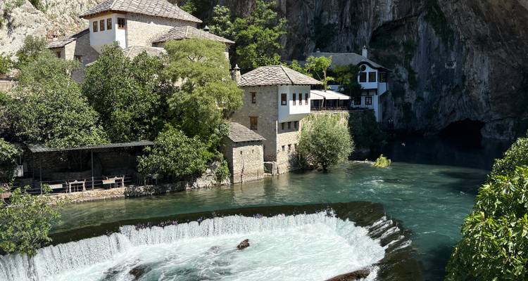 Monasterio histórico derviche y casas de piedra junto a un río turquesa que brota de un manantial en el acantilado.