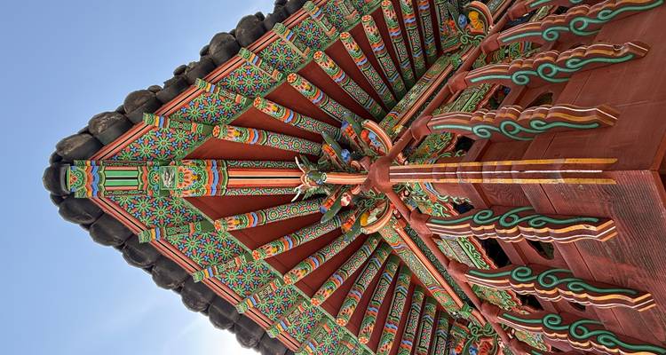 Des avant-toits en bois peints de manière intricate d'un temple coréen capturés de bas en haut contre un ciel bleu.