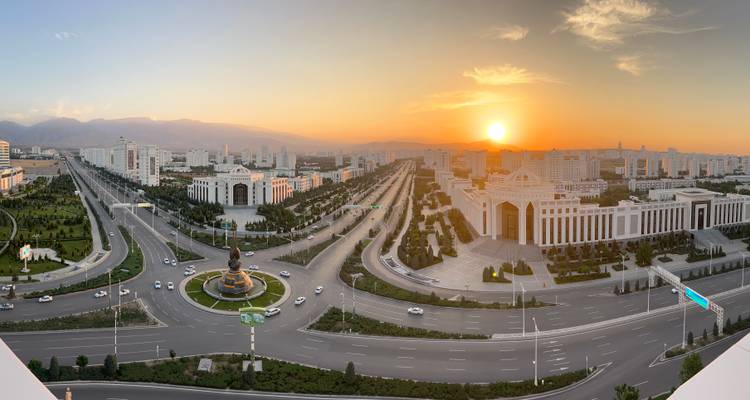 Panoramischer Sonnenuntergangsblick über eine prächtige, mit Marmor verkleidete moderne Stadt mit breiten Boulevards und der Sonne, die hinter entfernten Hügeln untergeht.
